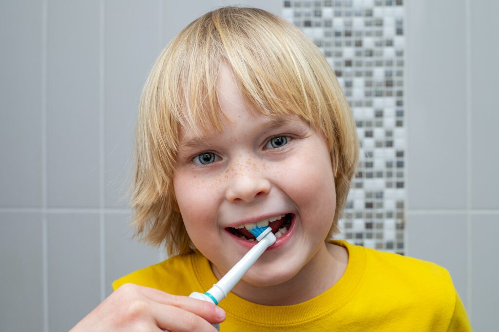 Little kid brushing his teeth with electric toothbrush in the bathroom