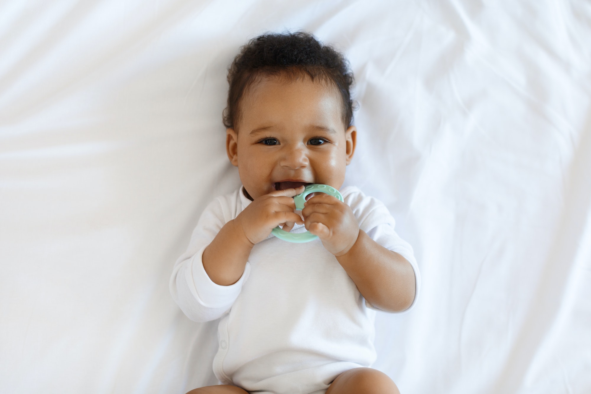 Portrait Of Adorable African American Baby Biting Teether And Looking At Camera