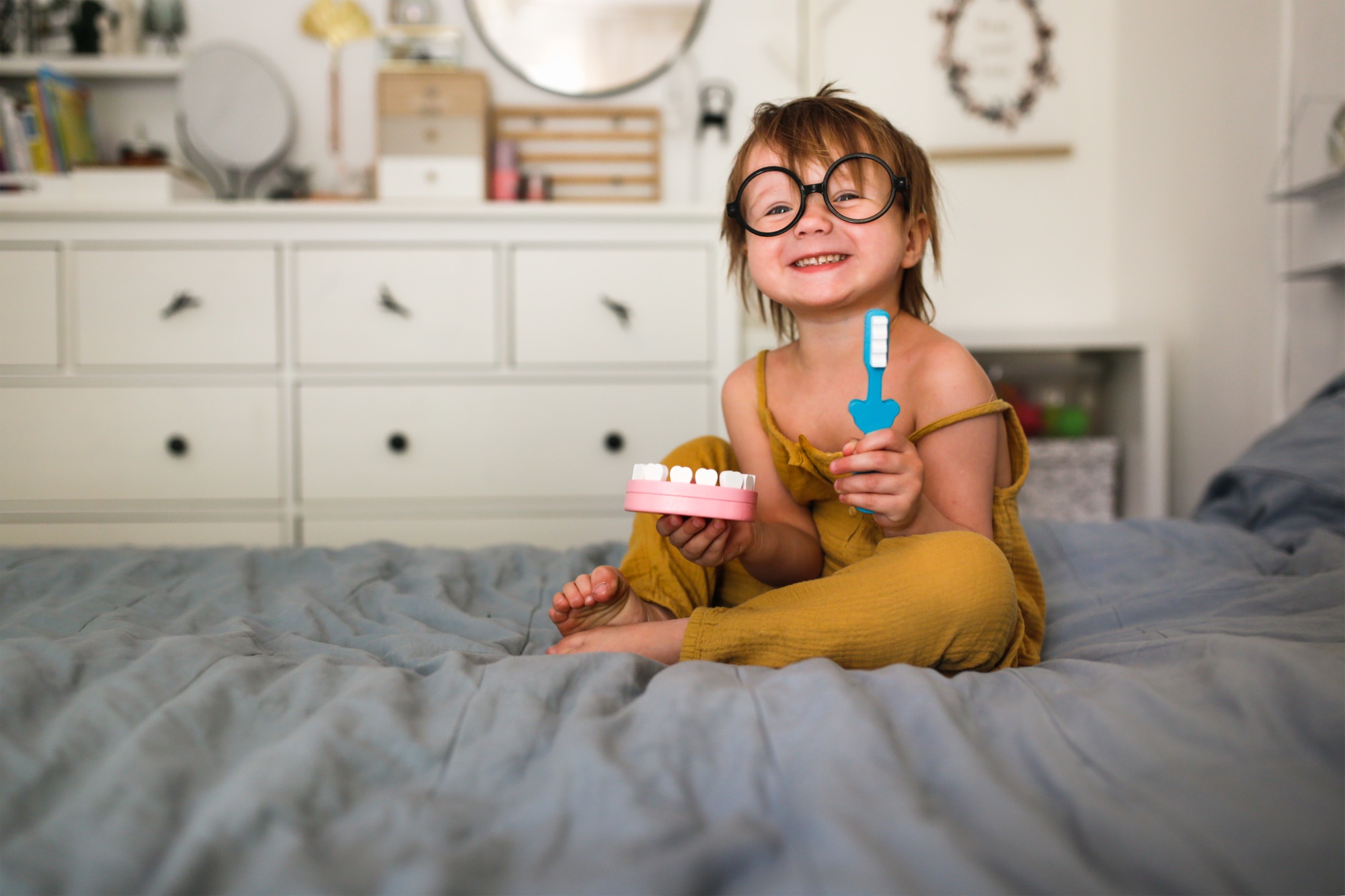 young child in glasses smiling and holding a dental model and toothbrush, promoting positive pediatric dental care at Salthouse Smiles in St. Louis, MO