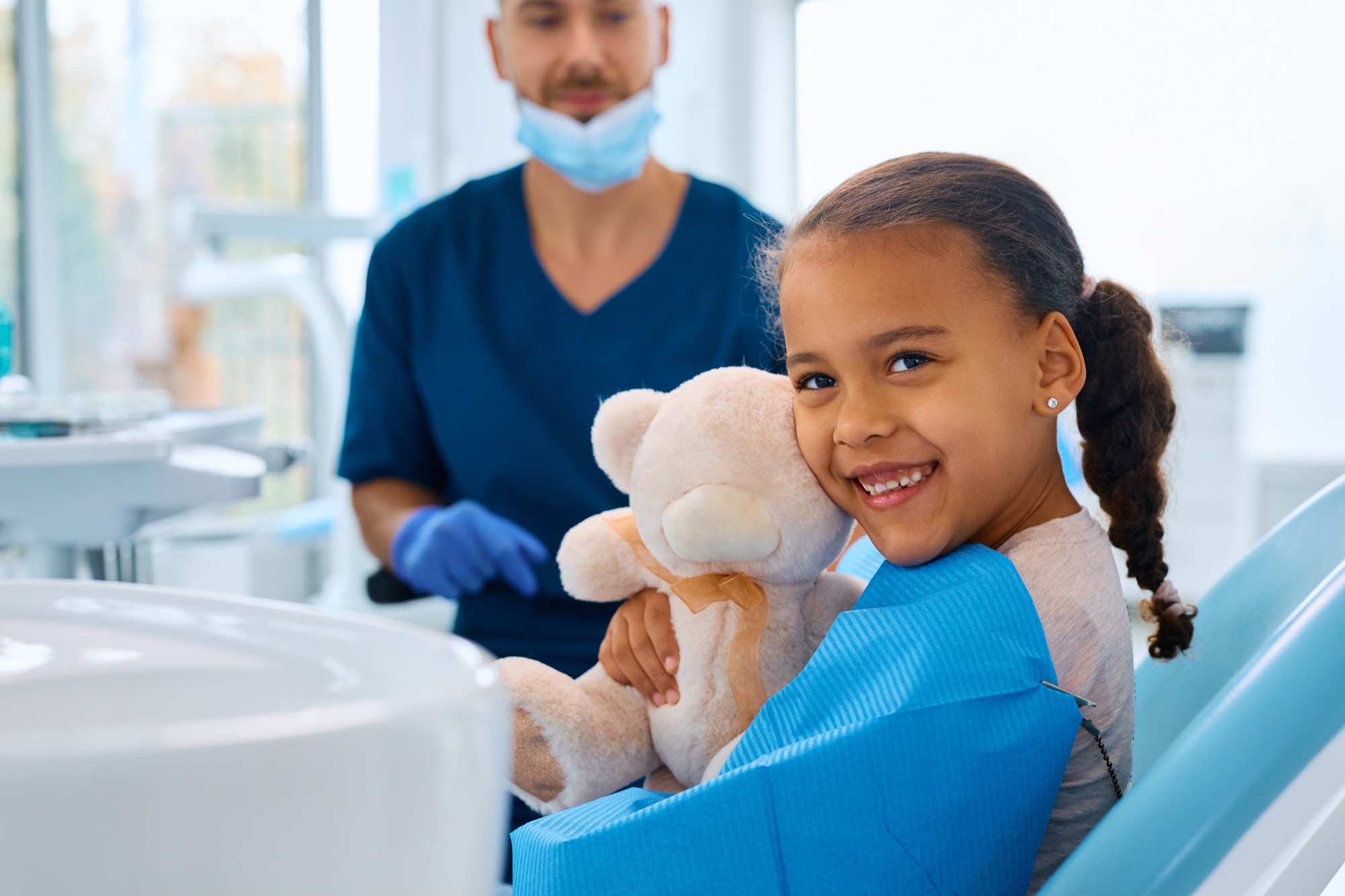 Smiling child holding teddy bear during dental visit with pediatric dentist in St. Louis.